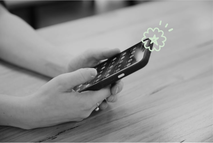 A black and white photo of a clse up of someones hands using a iphone