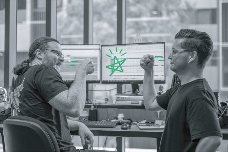A photo pf two men in front of a computer, they are fistbumping