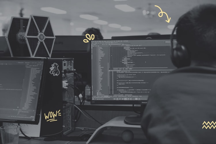 A photo of a man wearing headphones while working on a computer. His back is turned to the camera