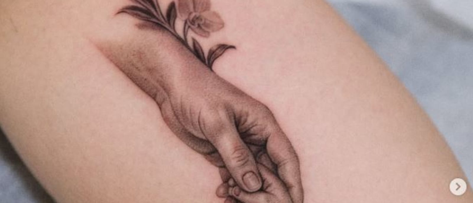 Fine-line tattoo of a hand holding flowers on an inner arm.