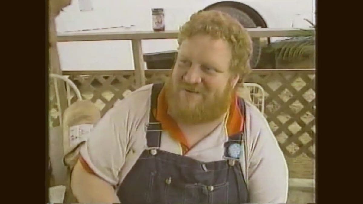 Video still of Jim Quessenberry in overalls on a lattice patio