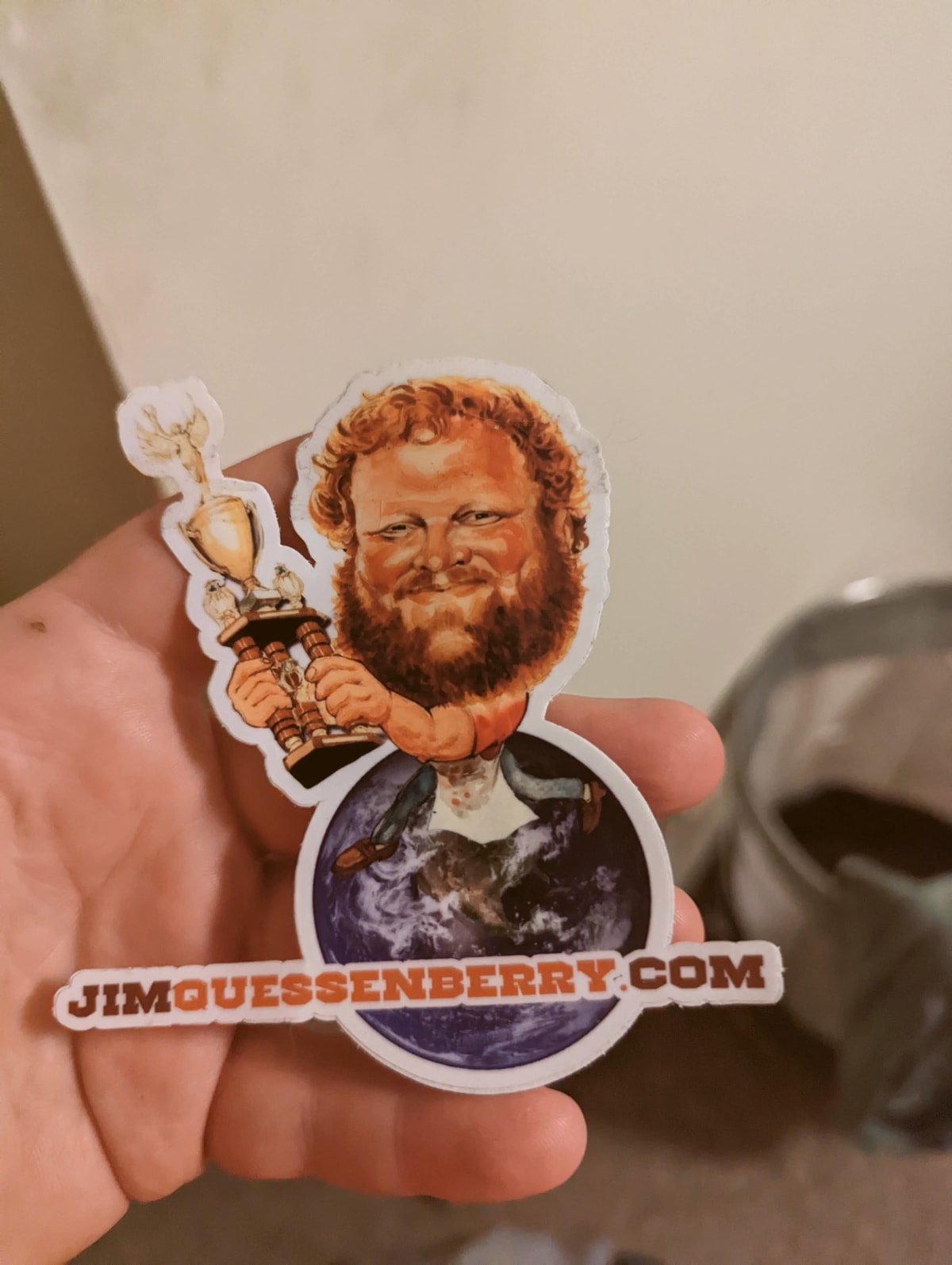 Hand holding a Jim Quessenberry caricature sticker