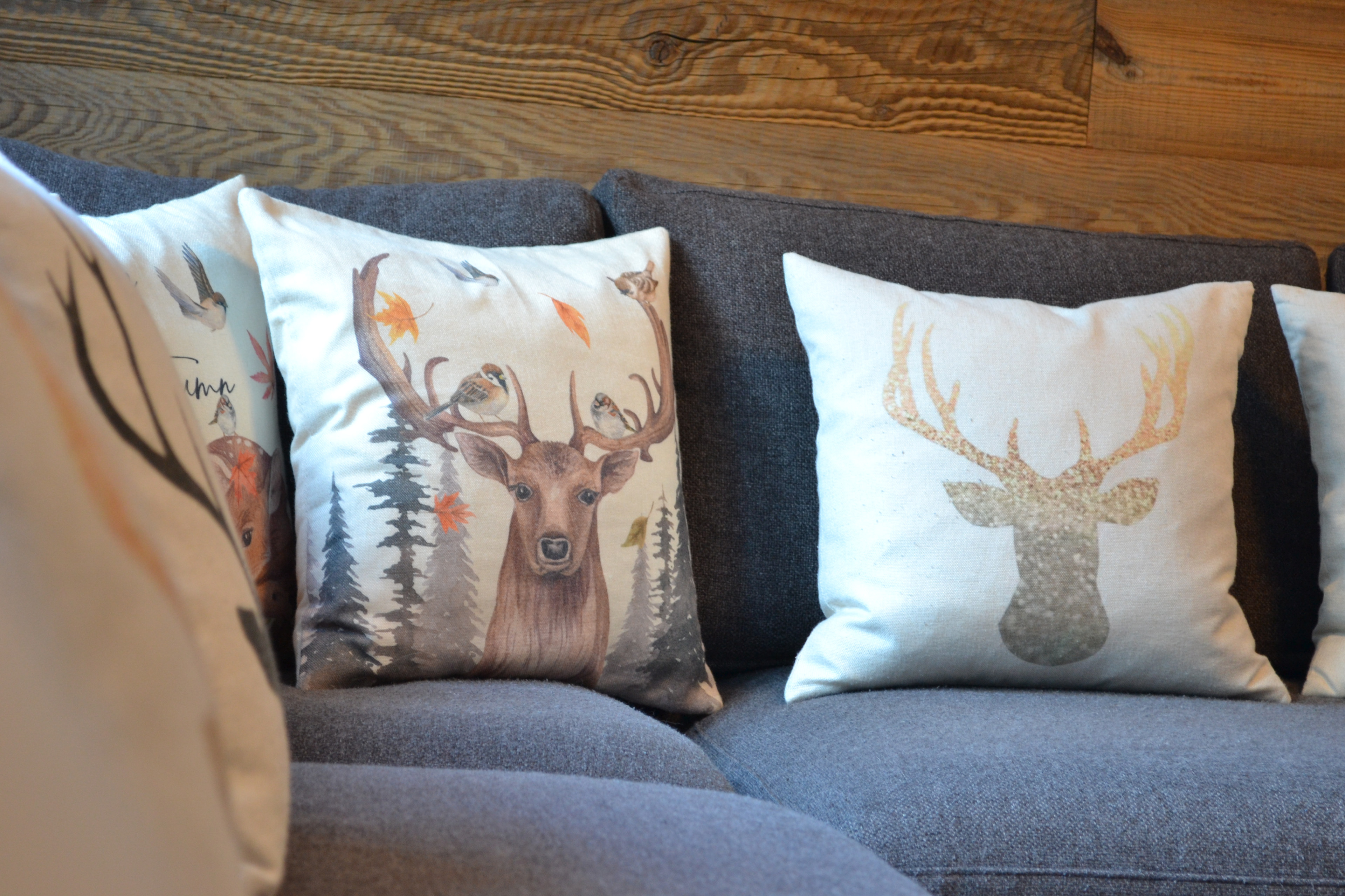 Gemütliche Sofaecke mit Hirschkissen vor Holzvertäfelung - alpine, warme Wohnatmosphäre