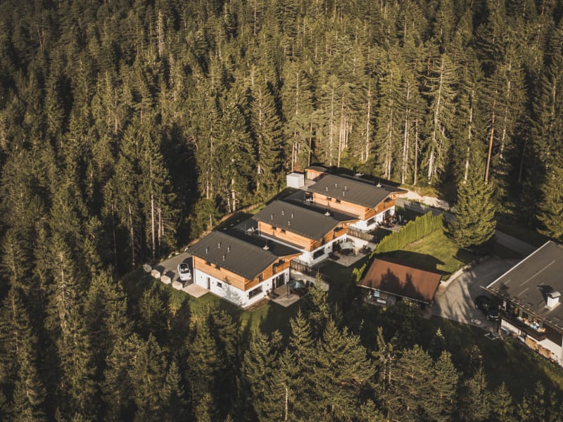 Wilderer Chalets – letecký snímek tří chaletů na zalesněném svahu – Leutasch, Tyrolsko