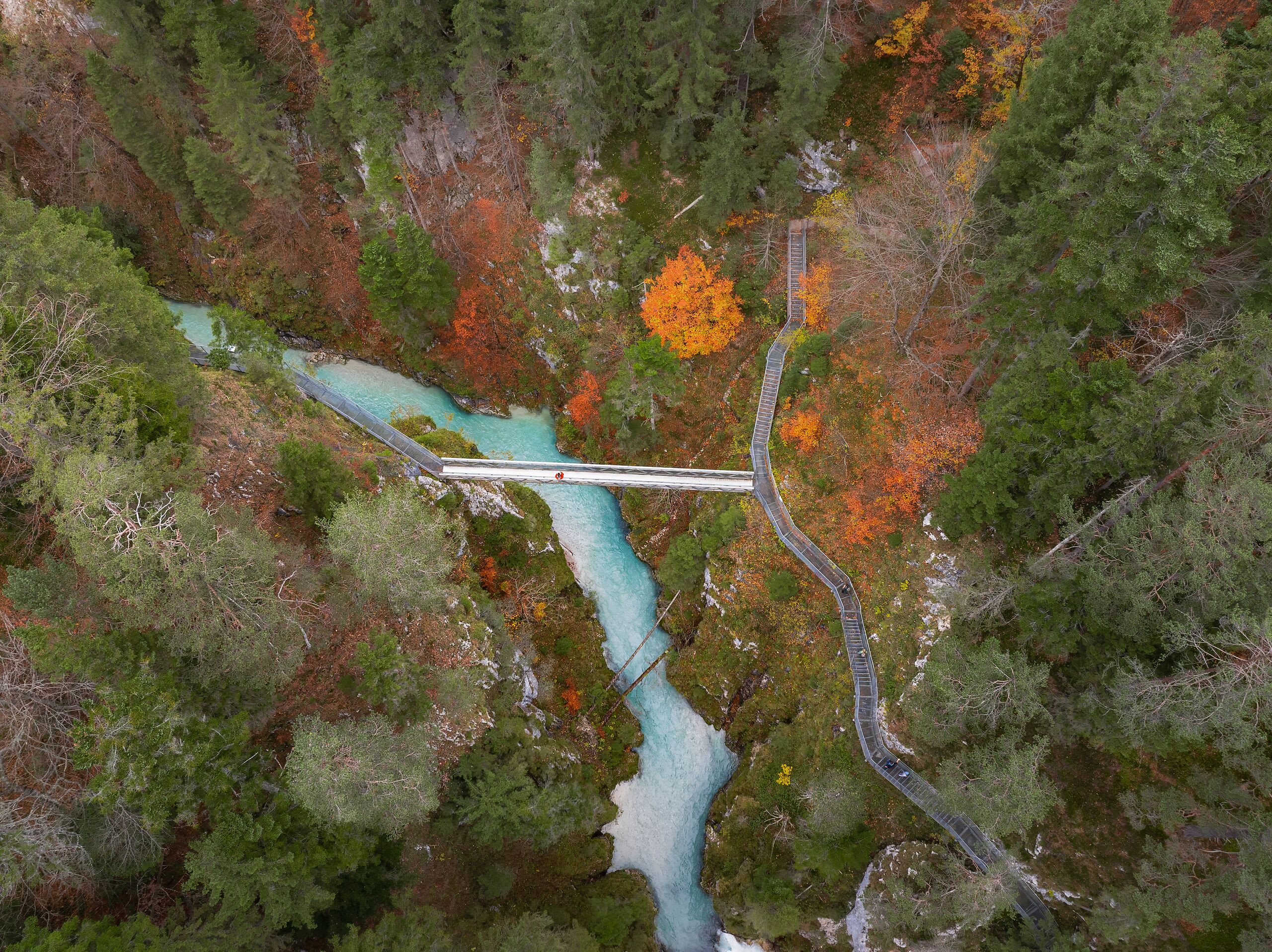 Droneoptagelse af Leutascher Geisterklamm i efteråret – mand i rød jakke på bro over kløften