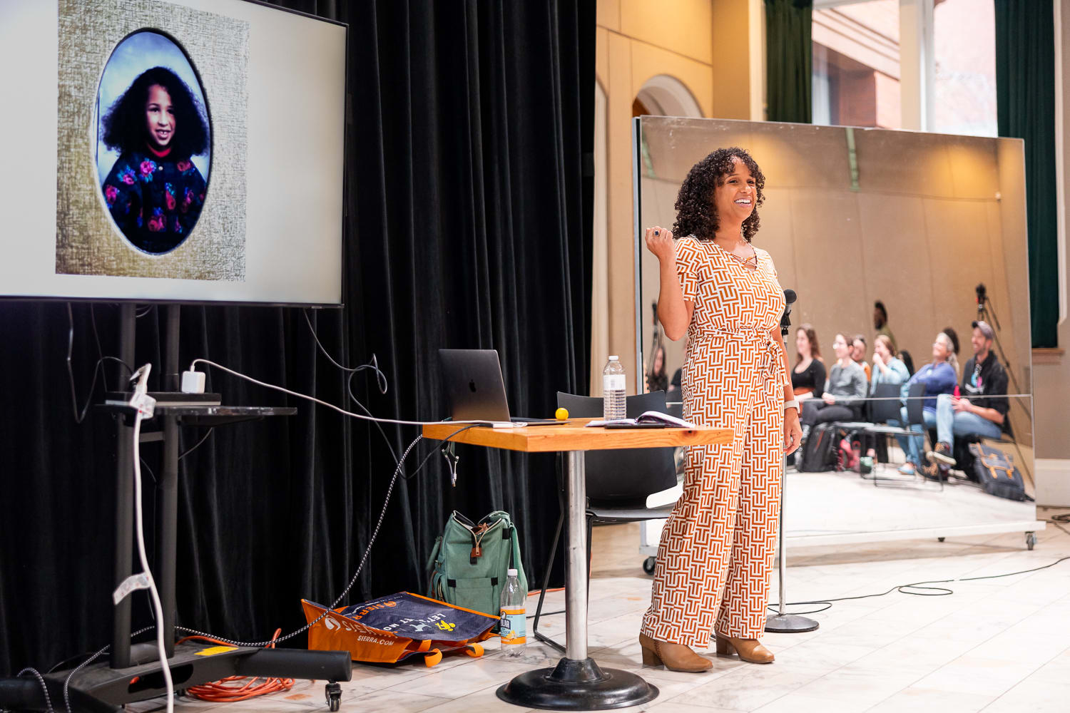 Kira Troilo speaking at the Black Hair Is Hair workshop, with a slide showing her childhood photo behind her.