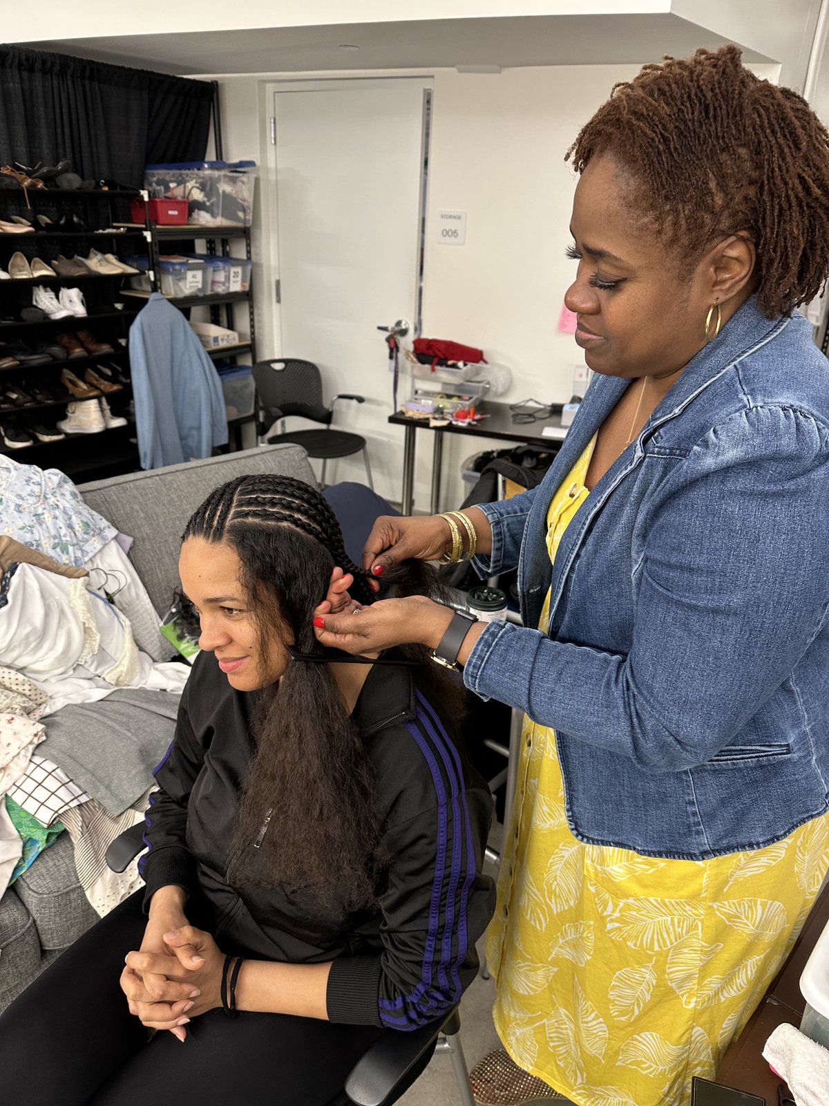 A licensed braider installing a protective style on a seated performer during Salon Day