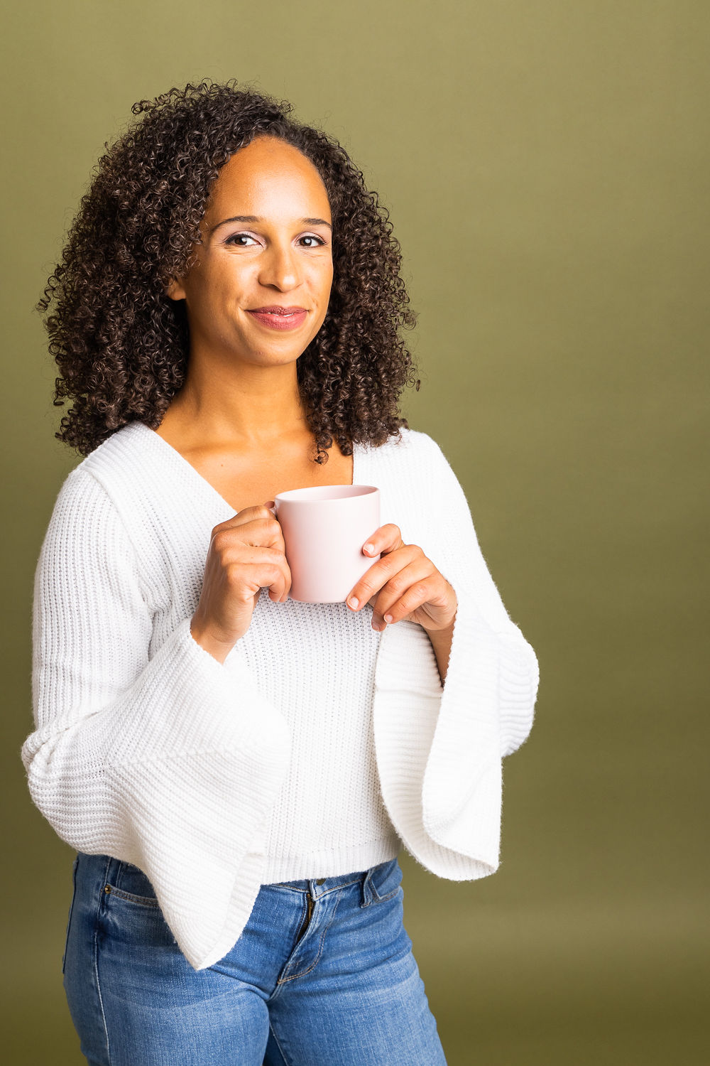 Kira Troilo, founder of Art & Soul Consulting, seated in a rattan peacock chair, smiling with a coffee mug in hand