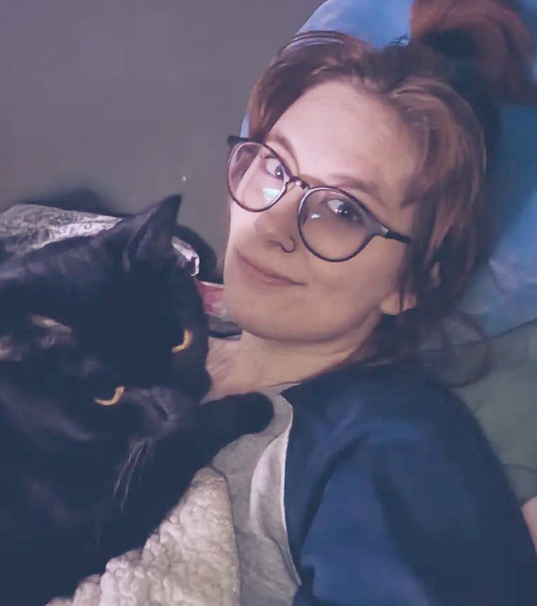 Charlie lying in bed with a black cat curled against her chest