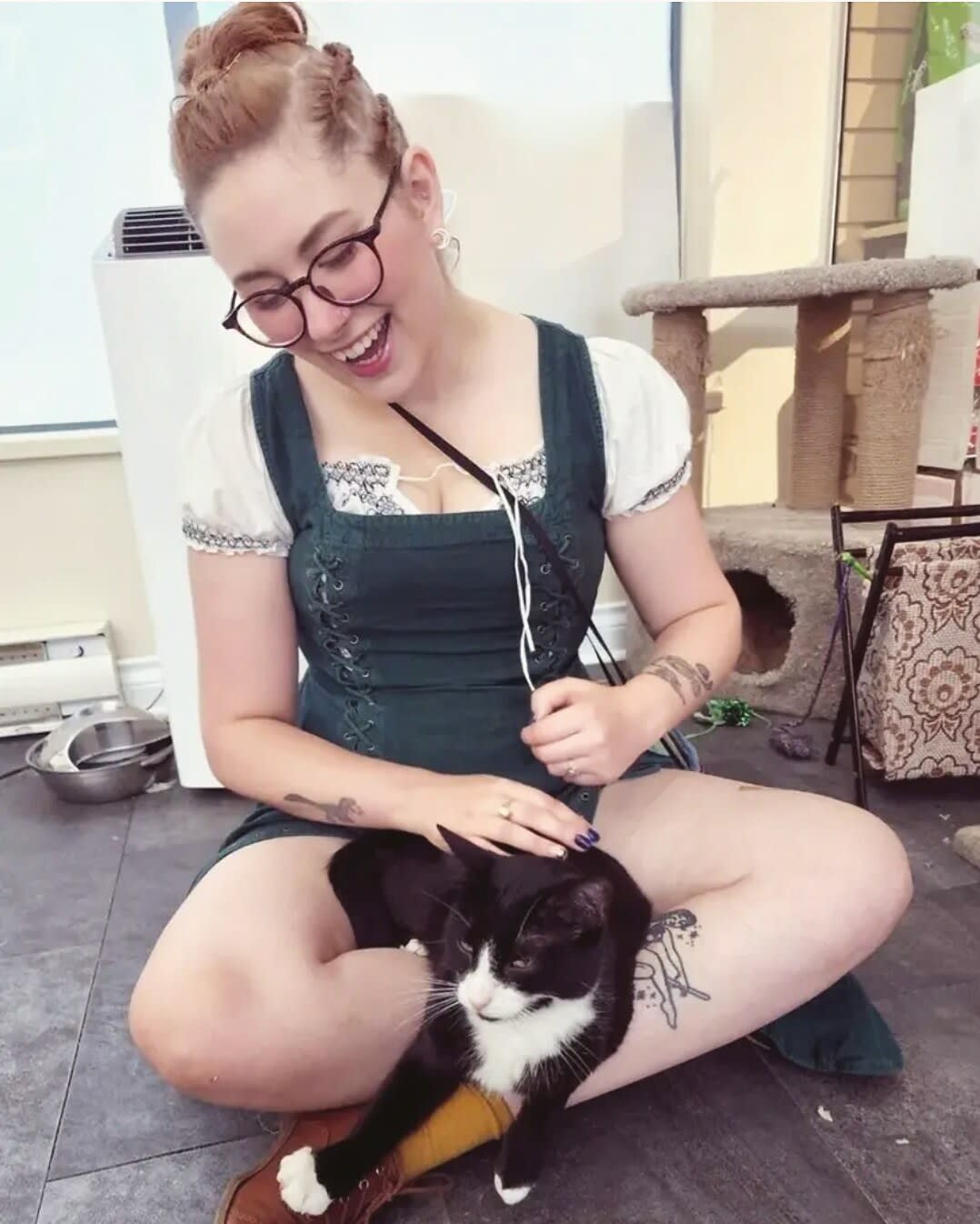 Charlie sitting cross-legged on a cat cafe floor, laughing while petting a tuxedo cat