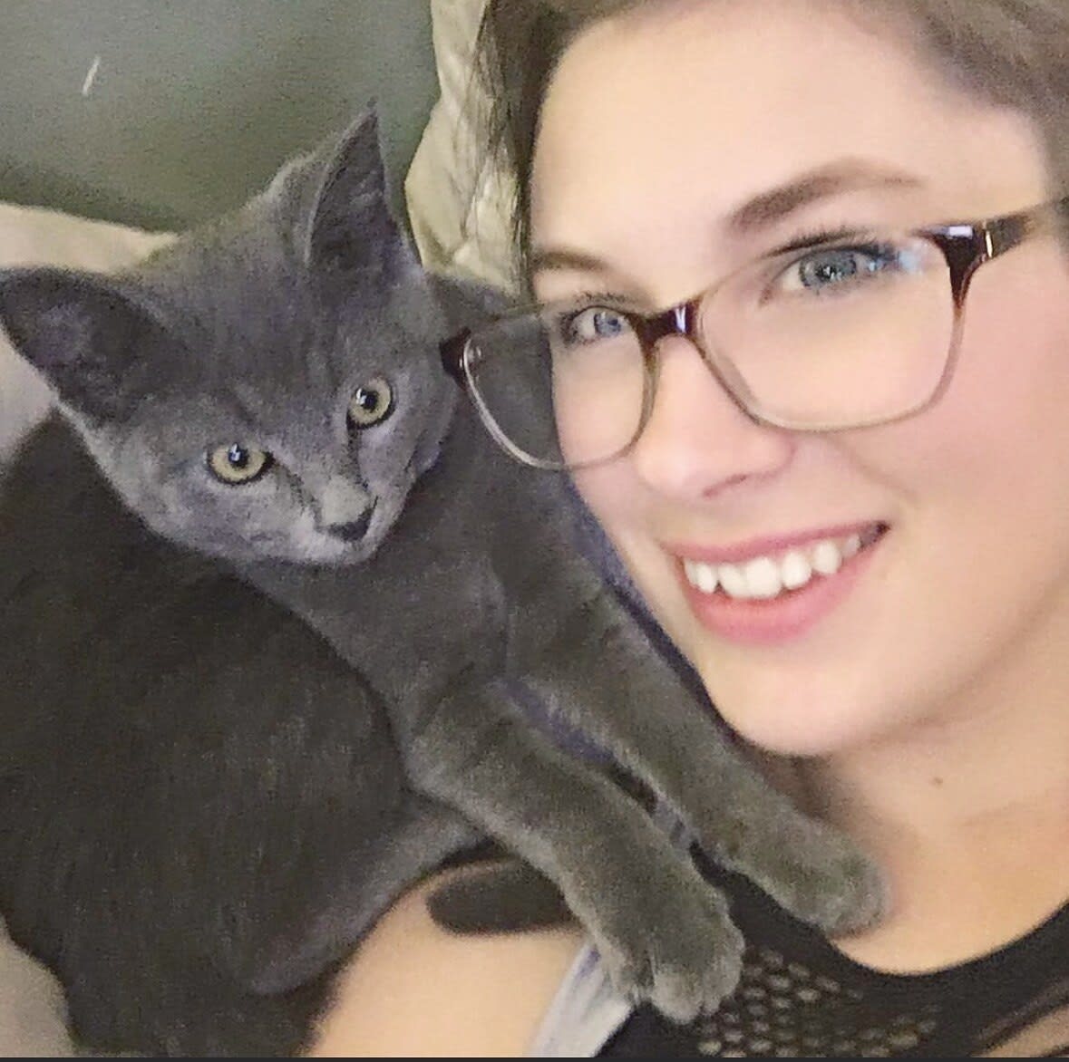 Charlie grinning with a grey kitten perched on her shoulder