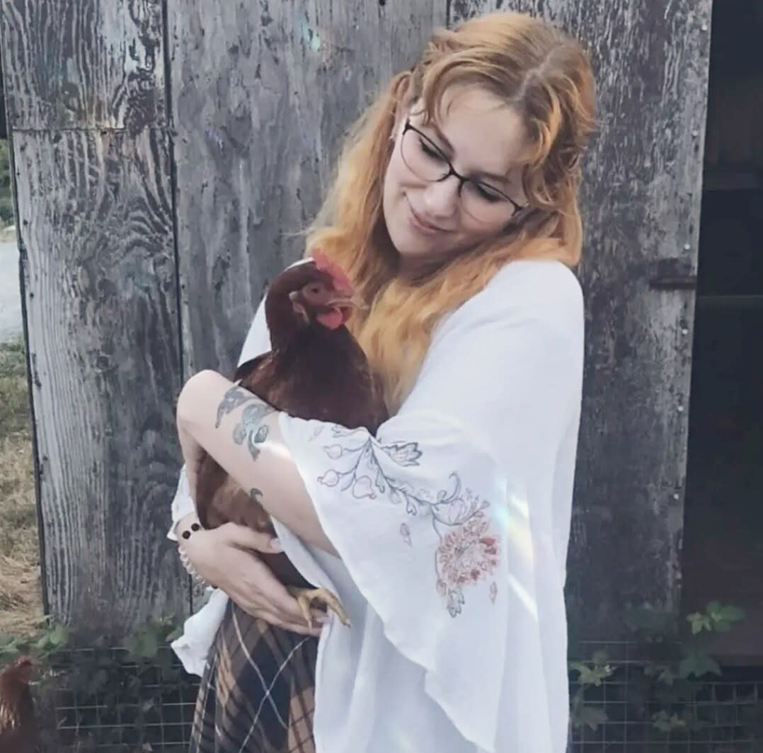 Charlie cradling a brown hen in her arms in front of a weathered barn