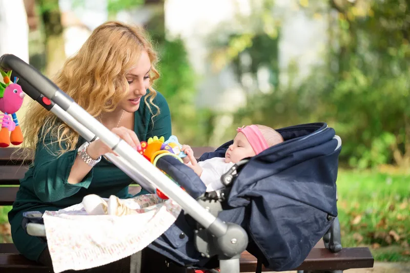 Woman taking care of her baby in a stroller while sitting on a bench in a park