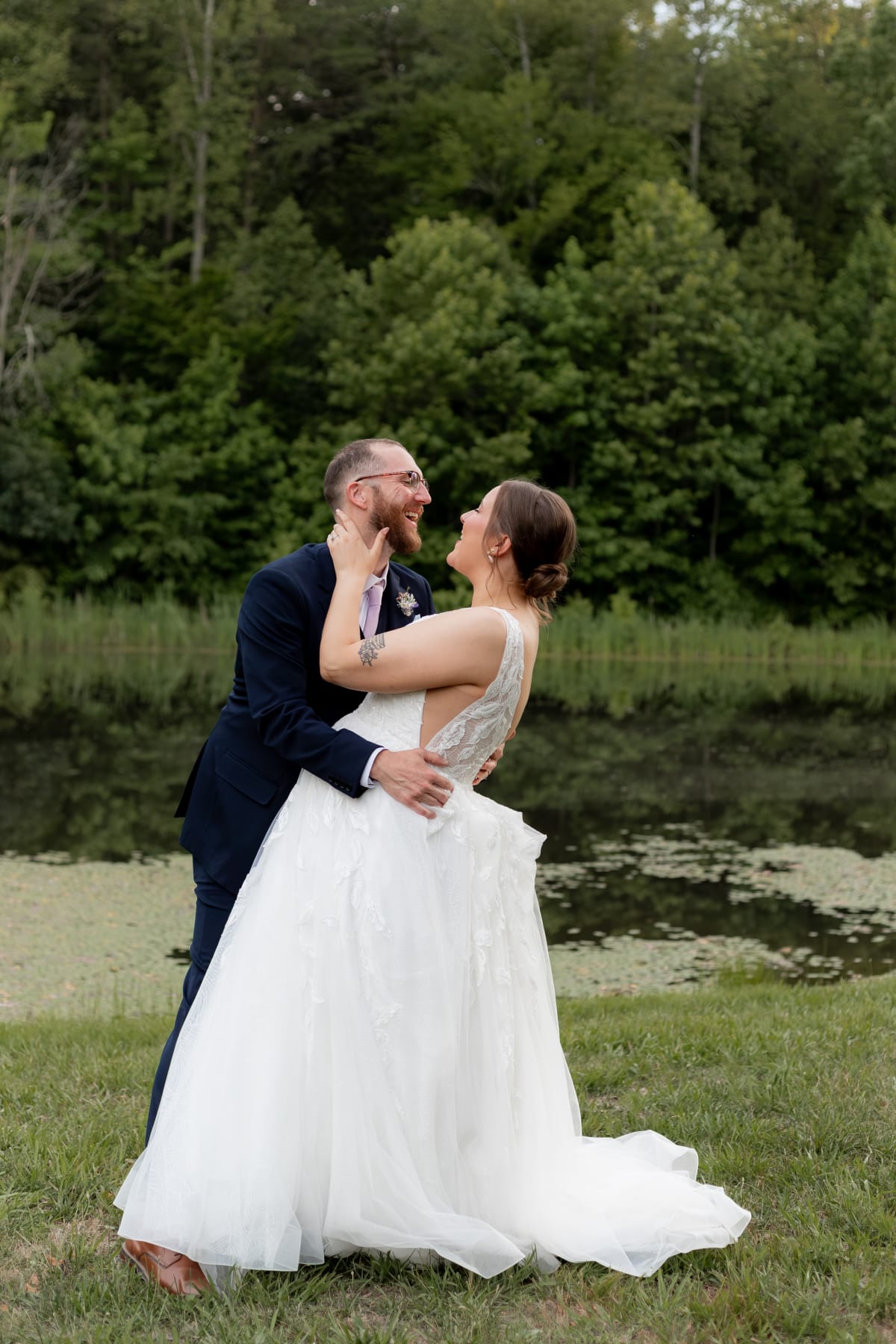 Couple laughing together during their Virginia microwedding, groom in navy suit and bride in lace gown near a lily pad pond