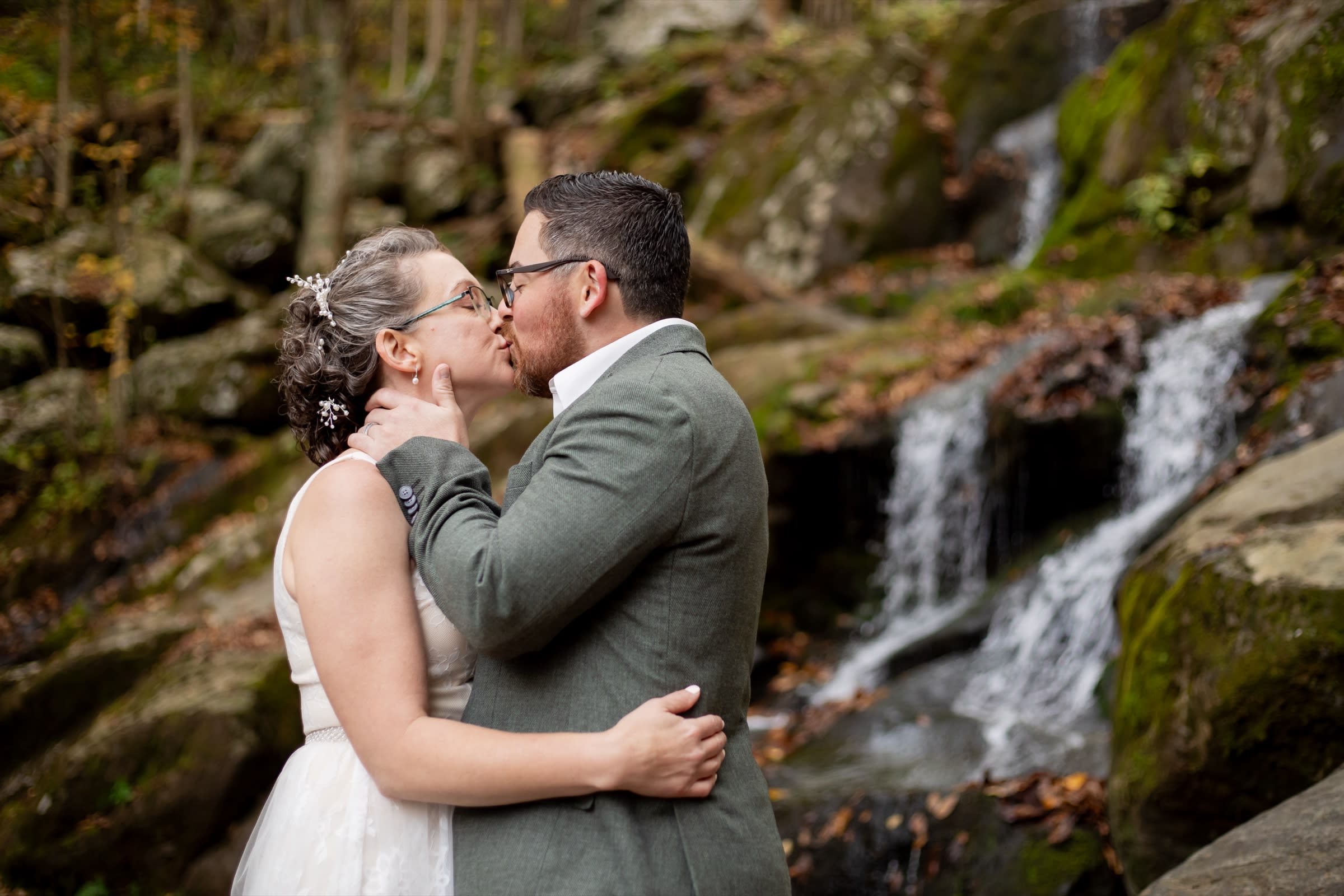 Couple kissing at Dark Hollow Falls in fall with moss-covered rocks and cascading water