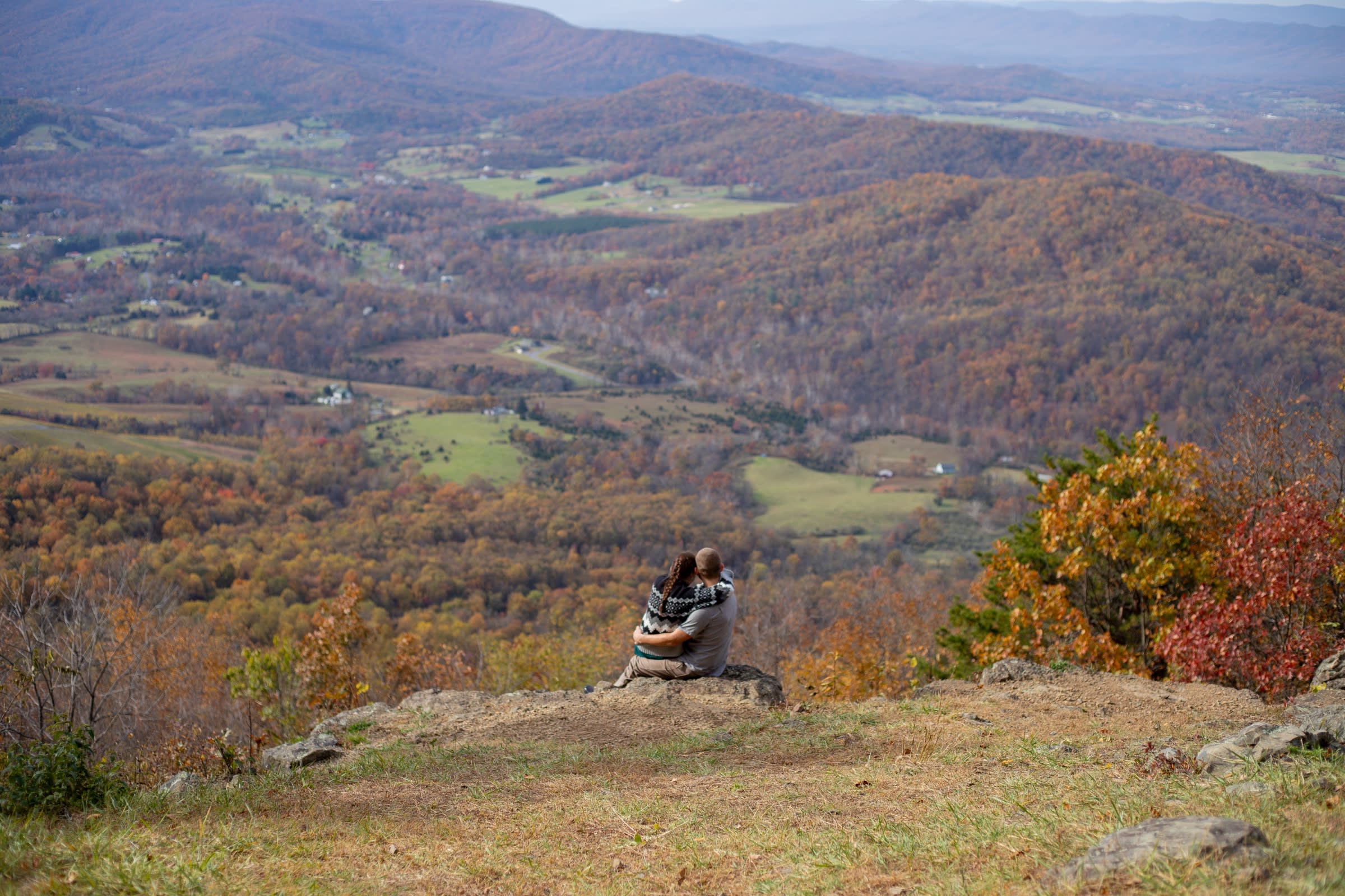 Couple sitting together on a rock overlooking the fall-colored valley at Snead Farm in Shenandoah National Park