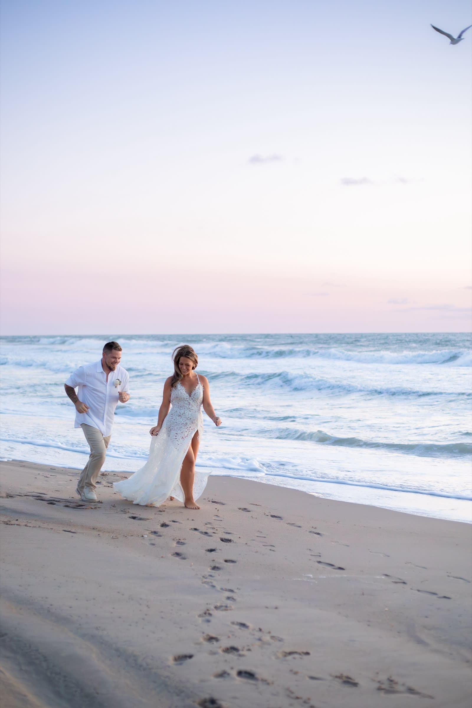 Couple running and laughing on a Virginia Beach shoreline at sunset with pink and purple sky