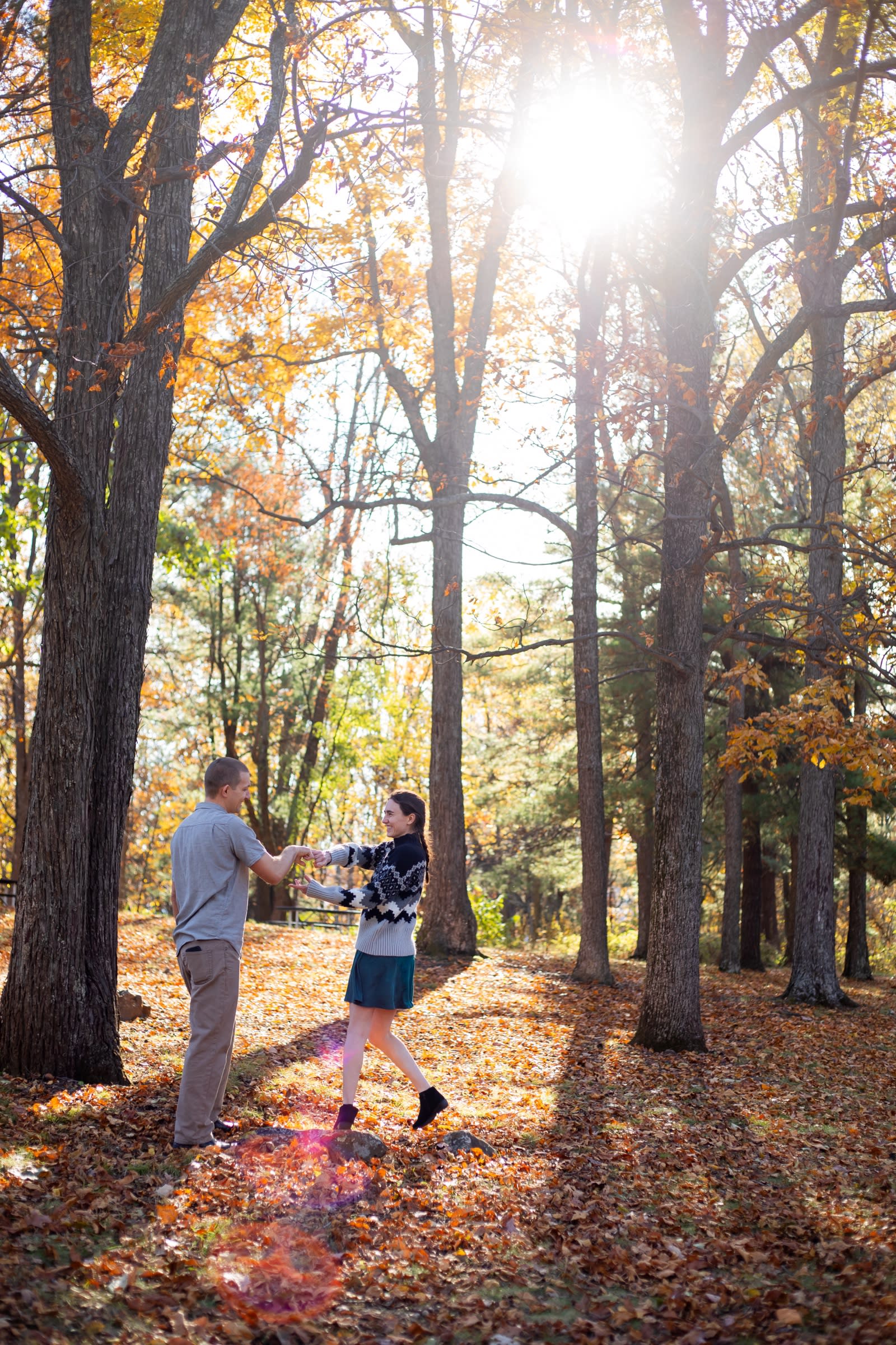 Couple dancing together under golden fall foliage with sunlight streaming through the trees at Snead Farm