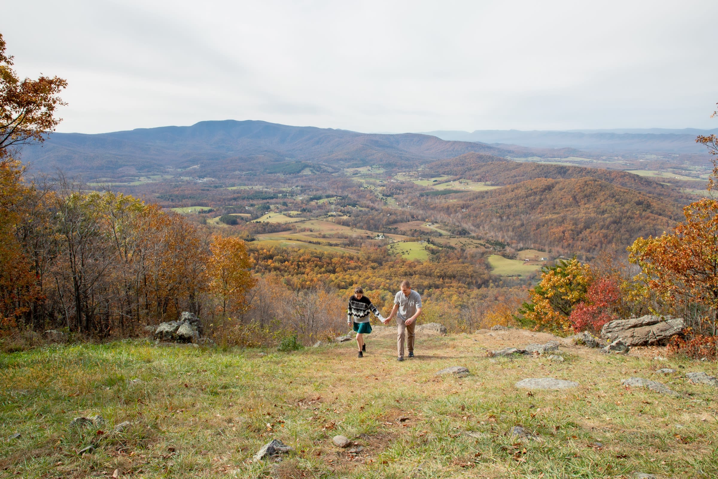 Couple walking down into a sweeping, hidden mountain overlook with fall foliage at Snead Farm in Shenandoah National Park