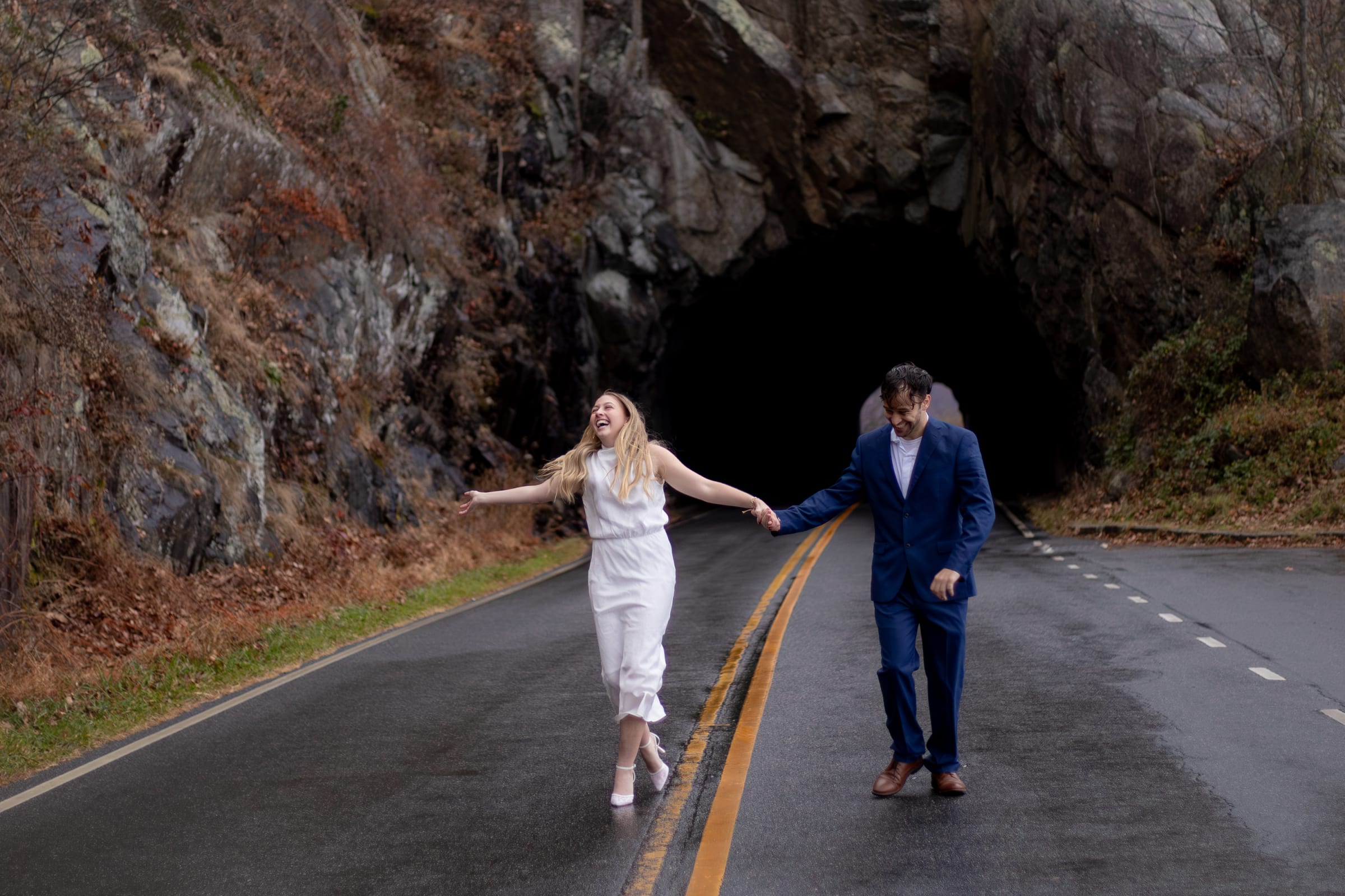 Couple laughing and walking hand in hand on a wet Skyline Drive road emerging from a tunnel, Shenandoah National Park