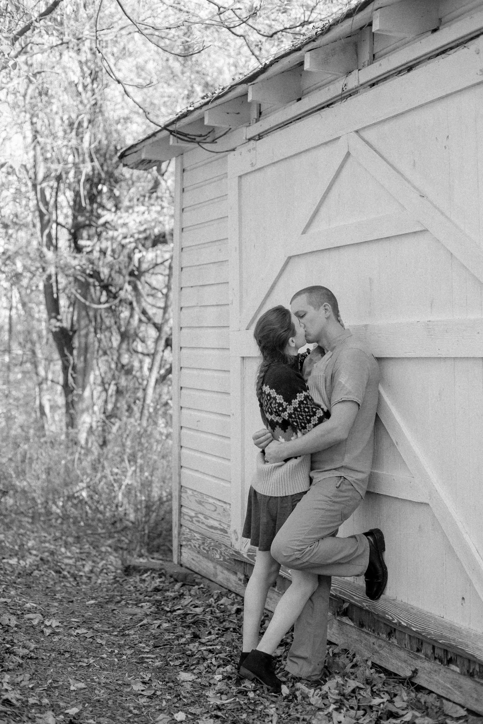 Black and white photo of a couple kissing beside the old barn at Snead Farm in Shenandoah National Park