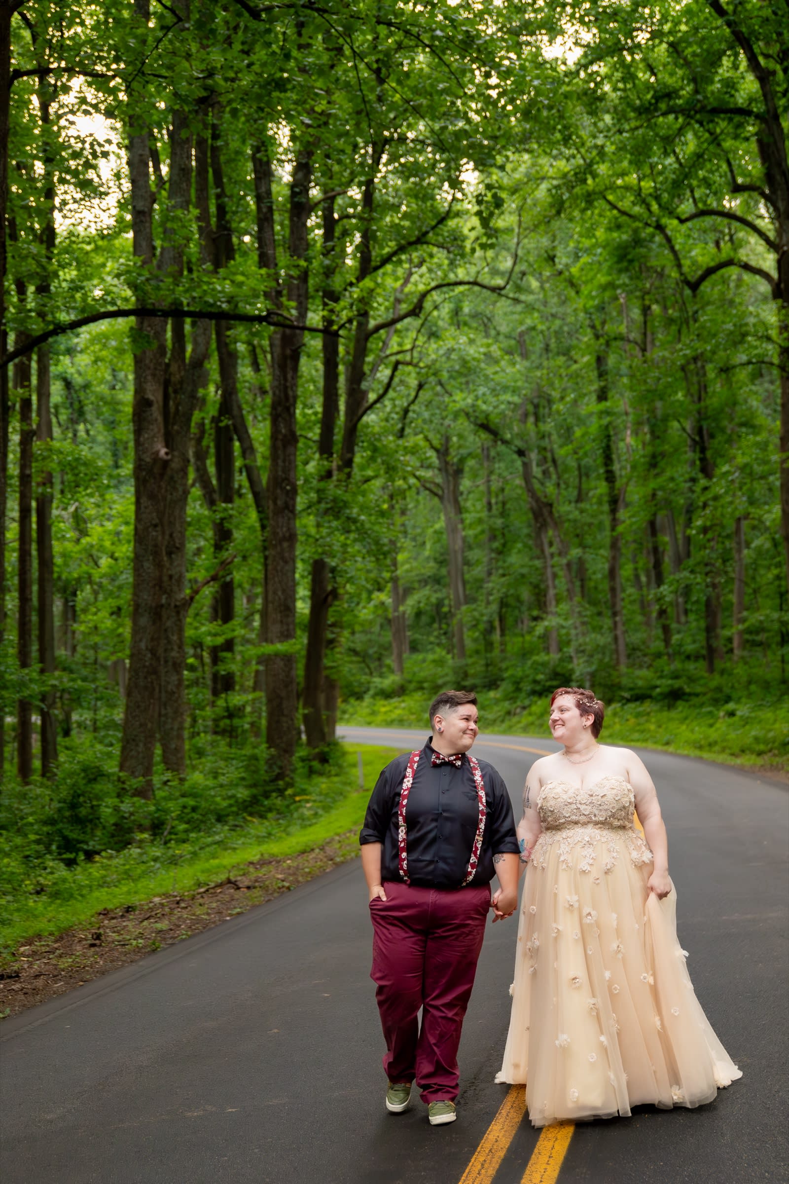 Couple walking hand in hand along a tree-lined road under a lush green summer canopy in Shenandoah National Park