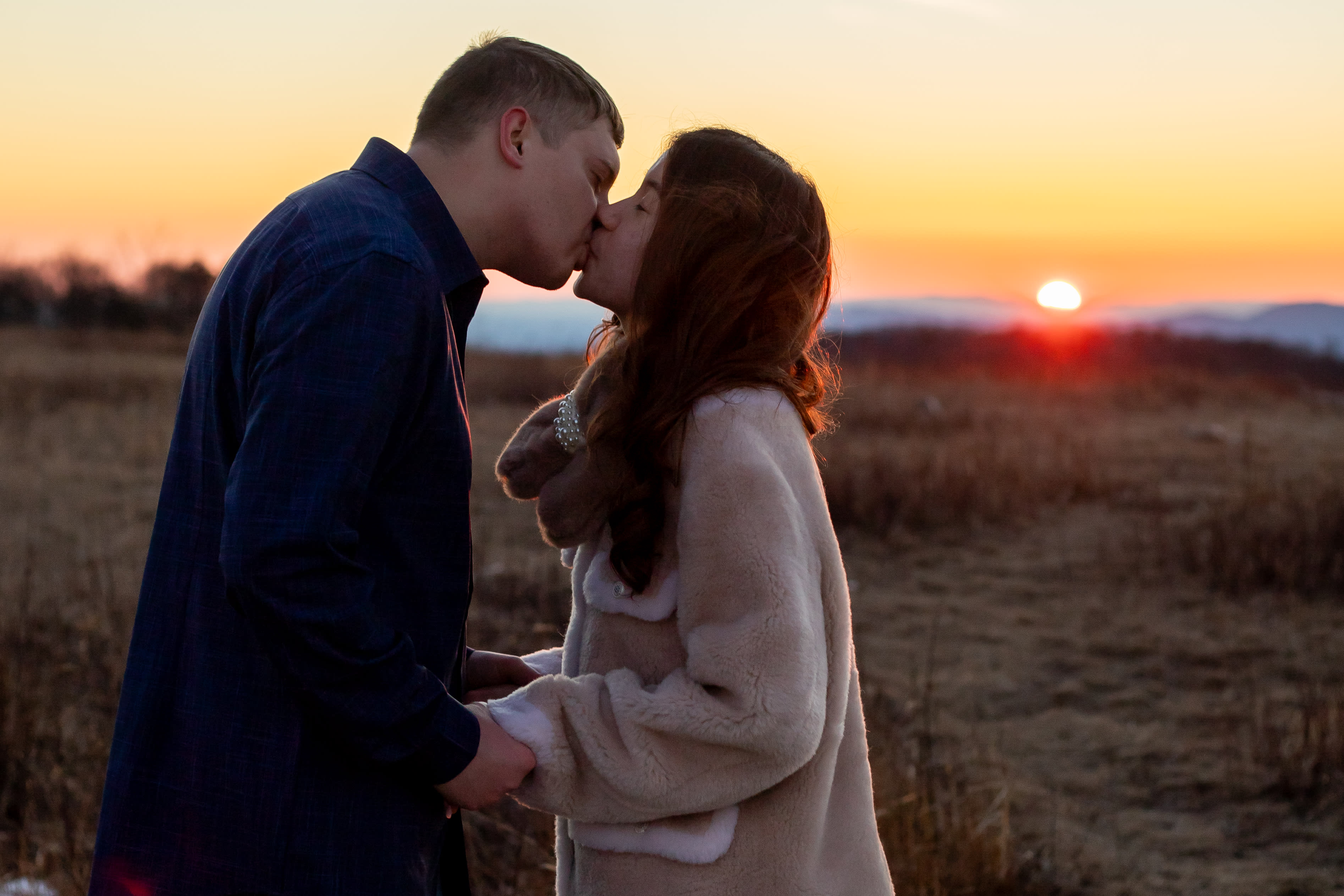 Couple kissing at sunset in the Big Meadows meadow in Shenandoah National Park, warm golden light on the horizon