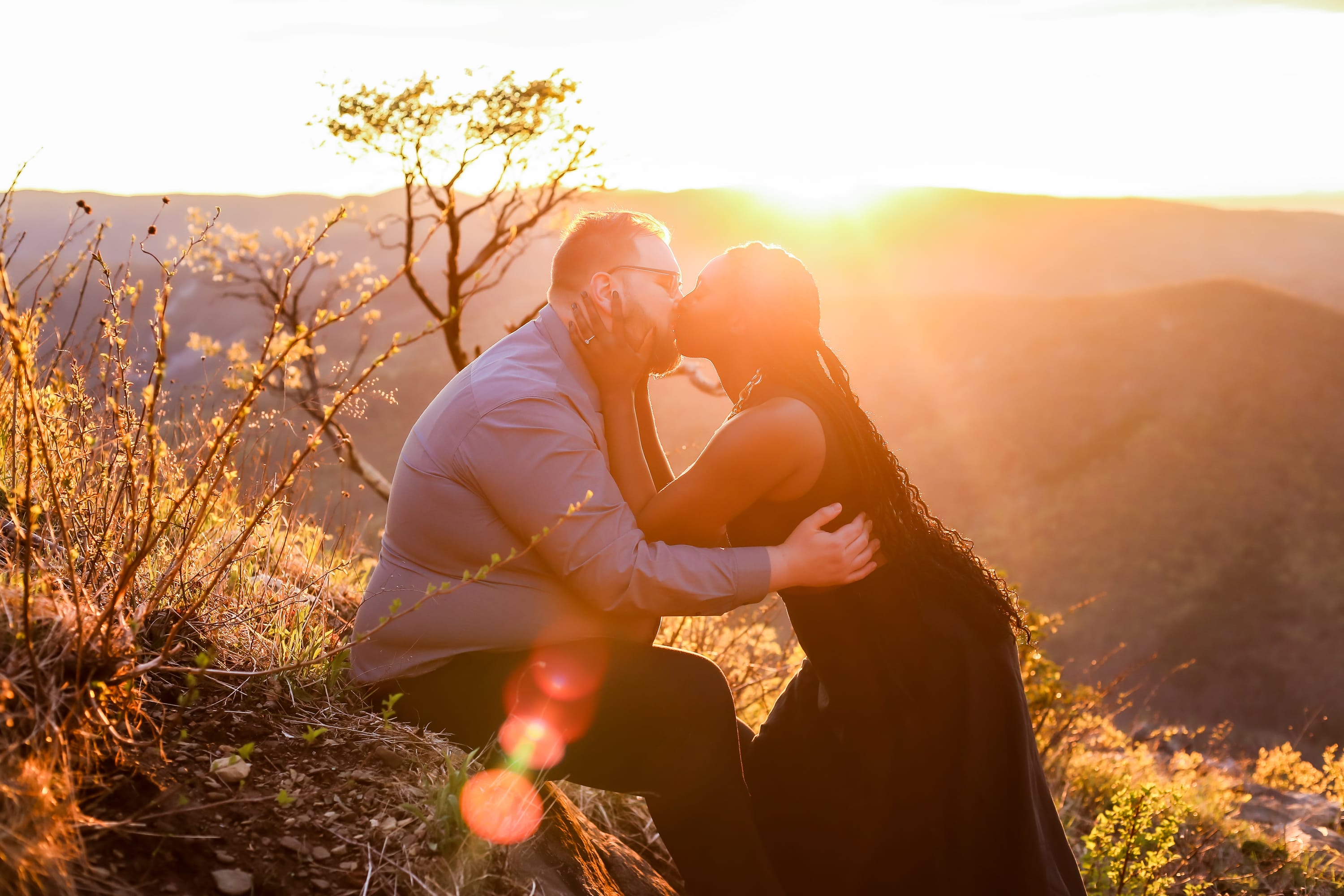 Couple sharing a kiss in golden light as the sun sets over the Blue Ridge Mountains at Raven's Roost Overlook, Virginia