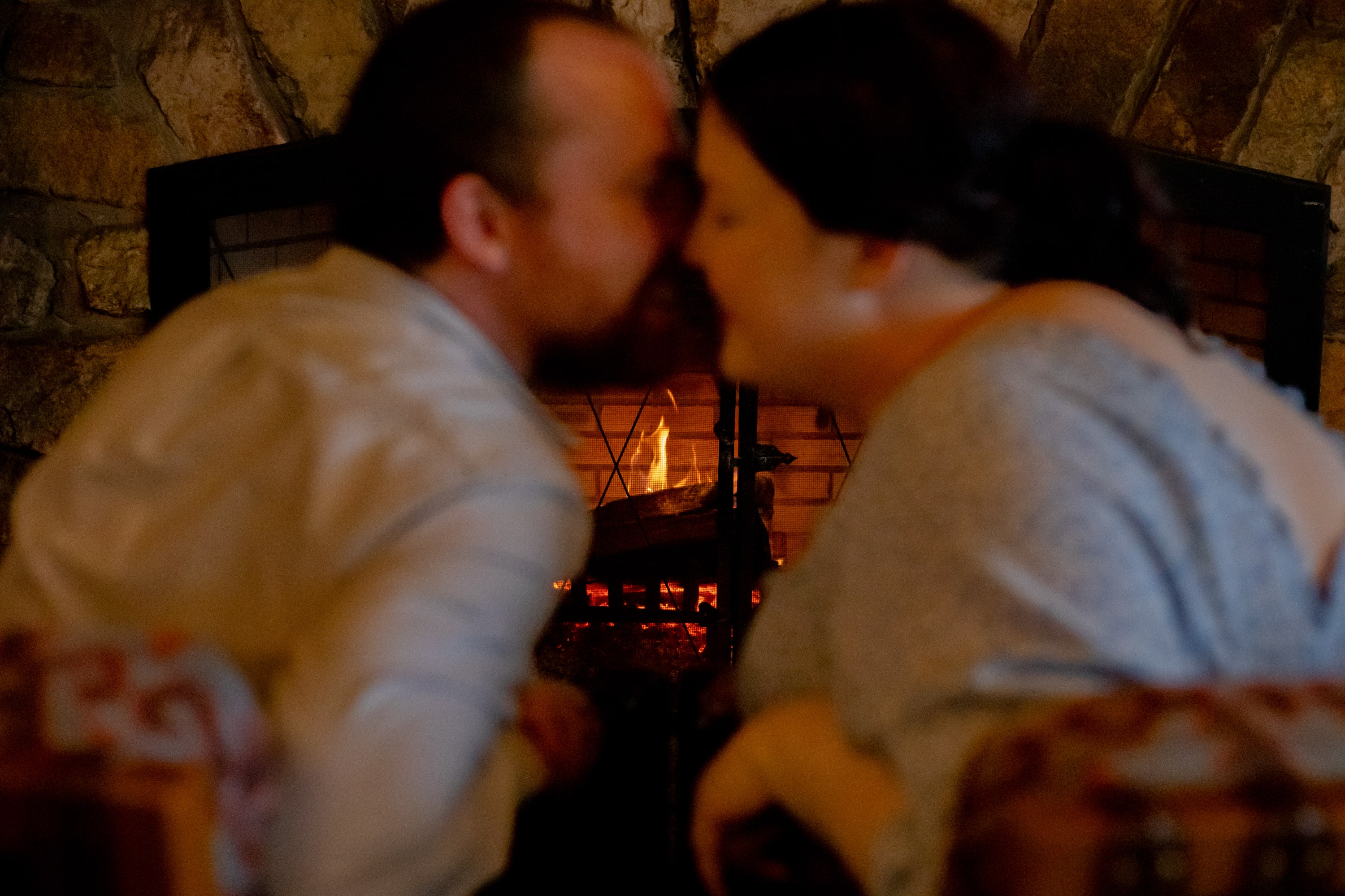 Couple leaning in for a kiss by the glowing fireplace inside Big Meadows Lodge, captured in black and white