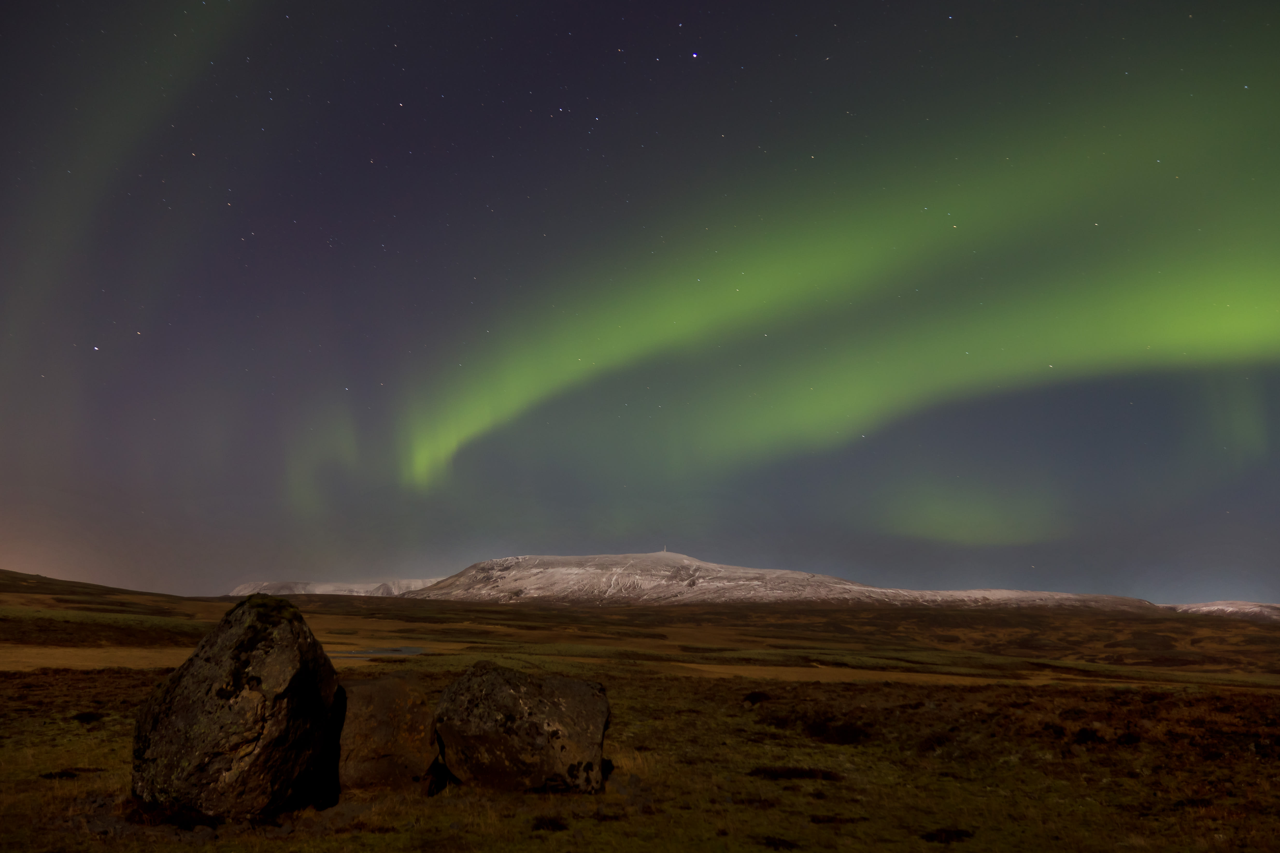 Aurora borealis over mountain with rock in foreground