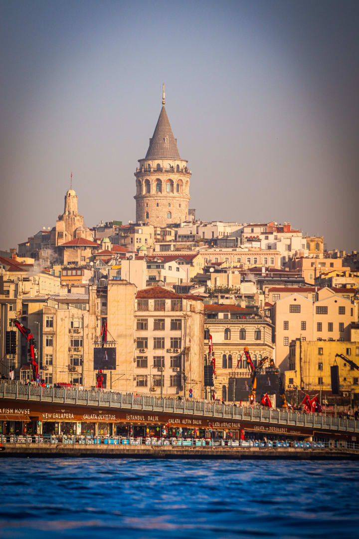 Galata Tower rising above the rooftops and Galata Bridge at golden hour in Istanbul