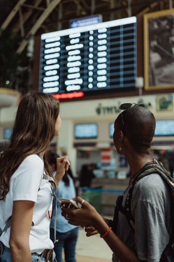 Two travellers checking a flight information board inside an airport terminal.