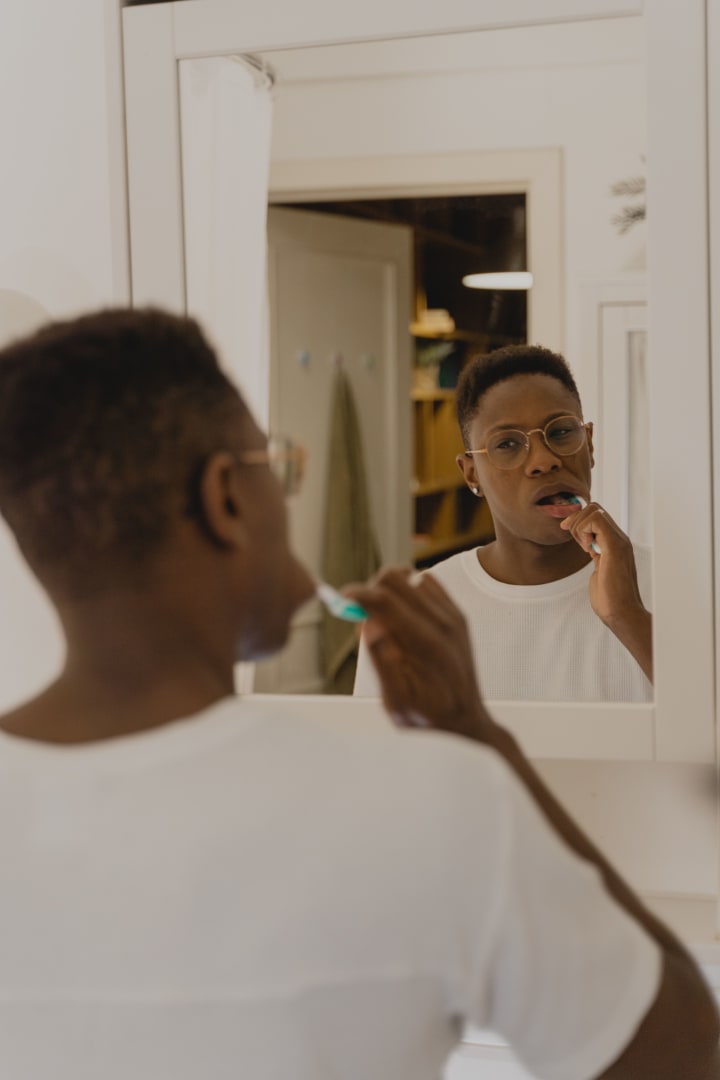 Adult man brushing his teeth in front of a bathroom mirror.