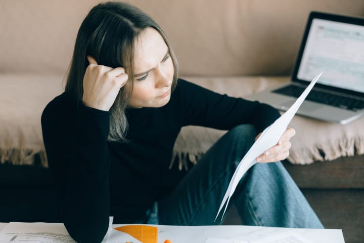 A woman reviewing printed documents beside an open laptop.