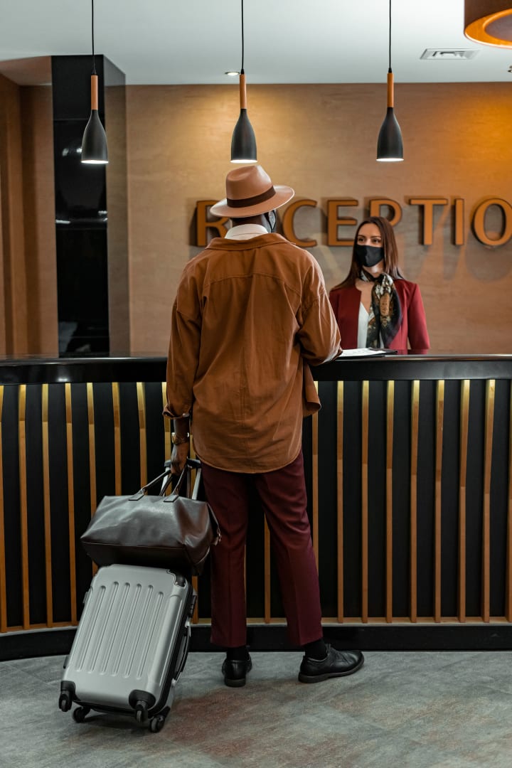 A traveller with luggage speaking to staff at a hotel reception desk.