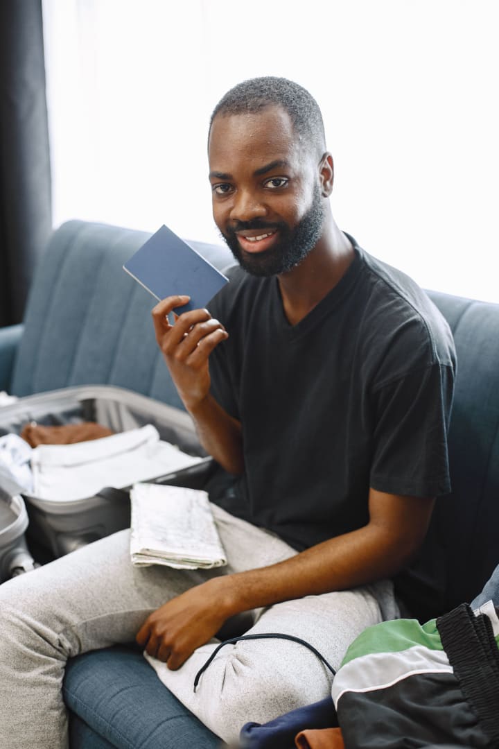 Adult packing a suitcase while holding a passport at home.