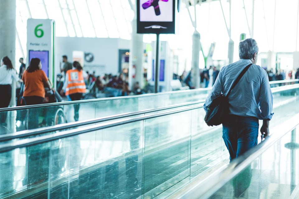 Travellers moving through a modern airport terminal on a moving walkway.
