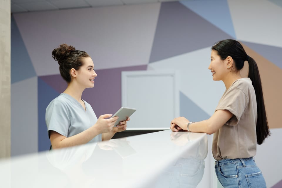 A receptionist speaking with a visitor at a modern reception desk.