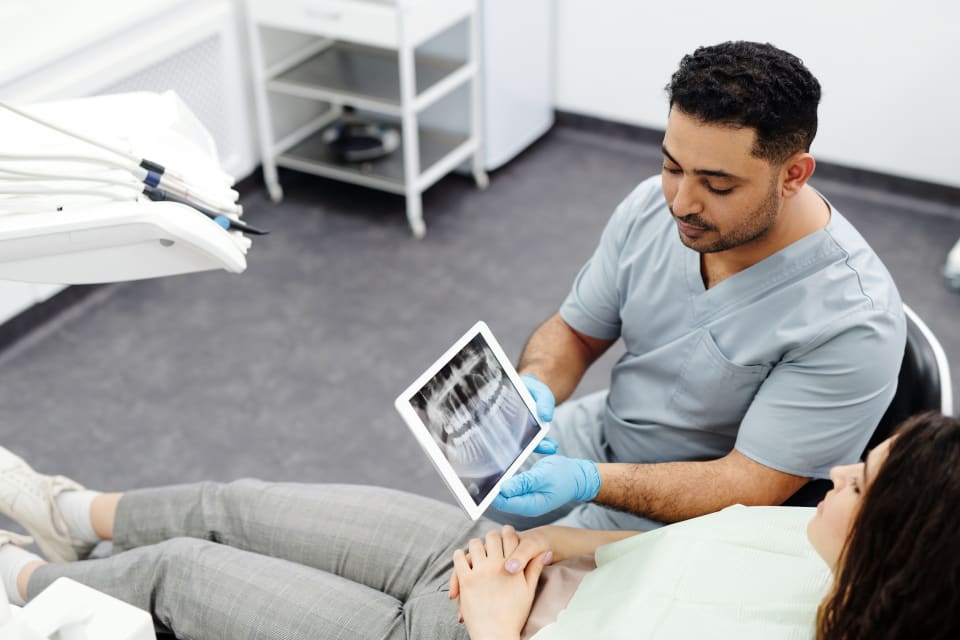 Dentist showing a dental X-ray to a patient on a tablet during a treatment-planning consultation
