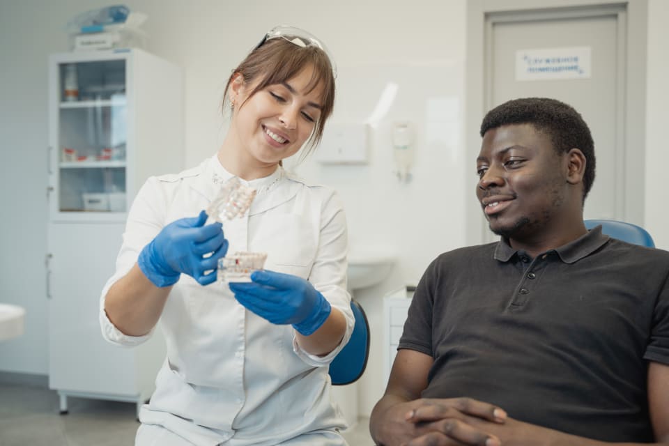 Smiling dentist shows dental model to relaxed patient during consultation at clinic.