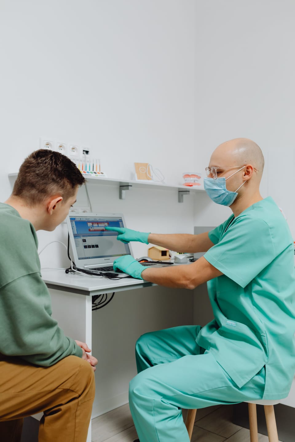 Dentist consulting a patient while reviewing dental information on a laptop.