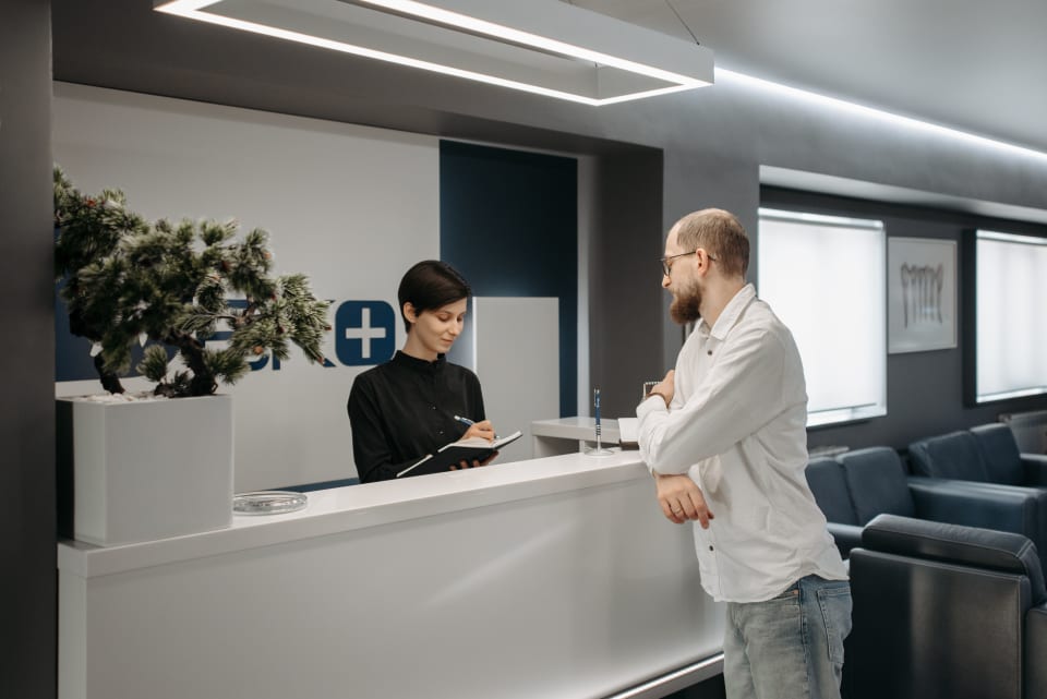 A patient discussing practical arrangements with a reception coordinator in a modern healthcare setting.