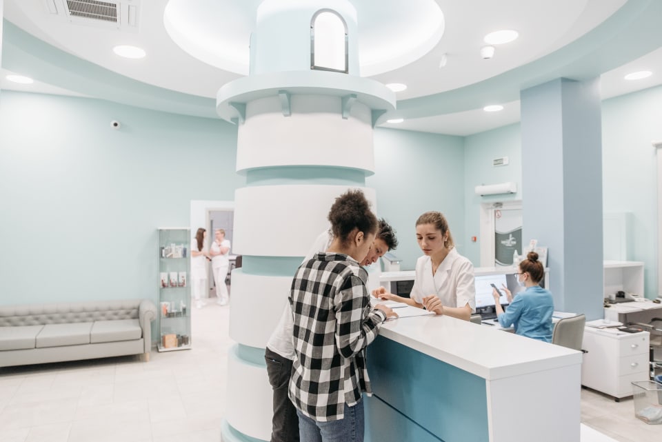 Adults speaking with reception staff in a bright healthcare setting.