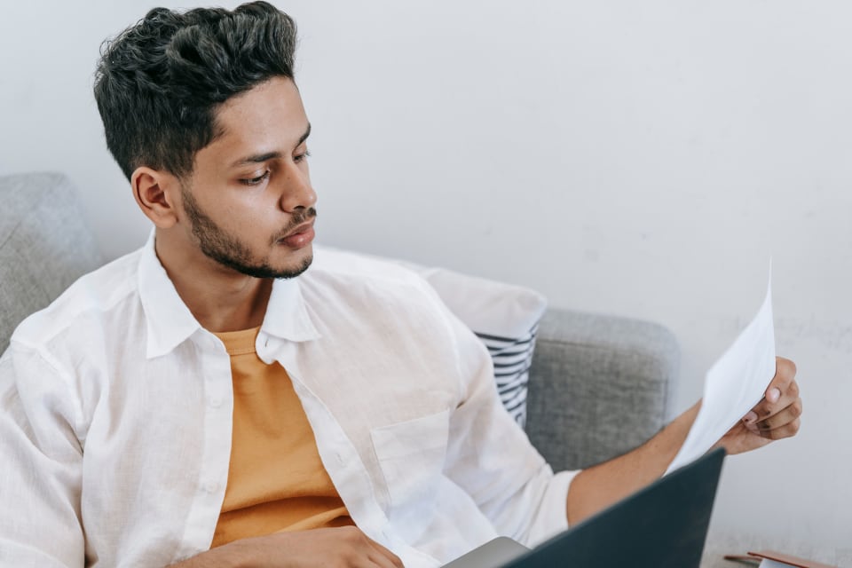 Person reading a document while using a laptop at home.