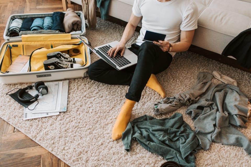 Traveller using a laptop while packing a suitcase at home before departure