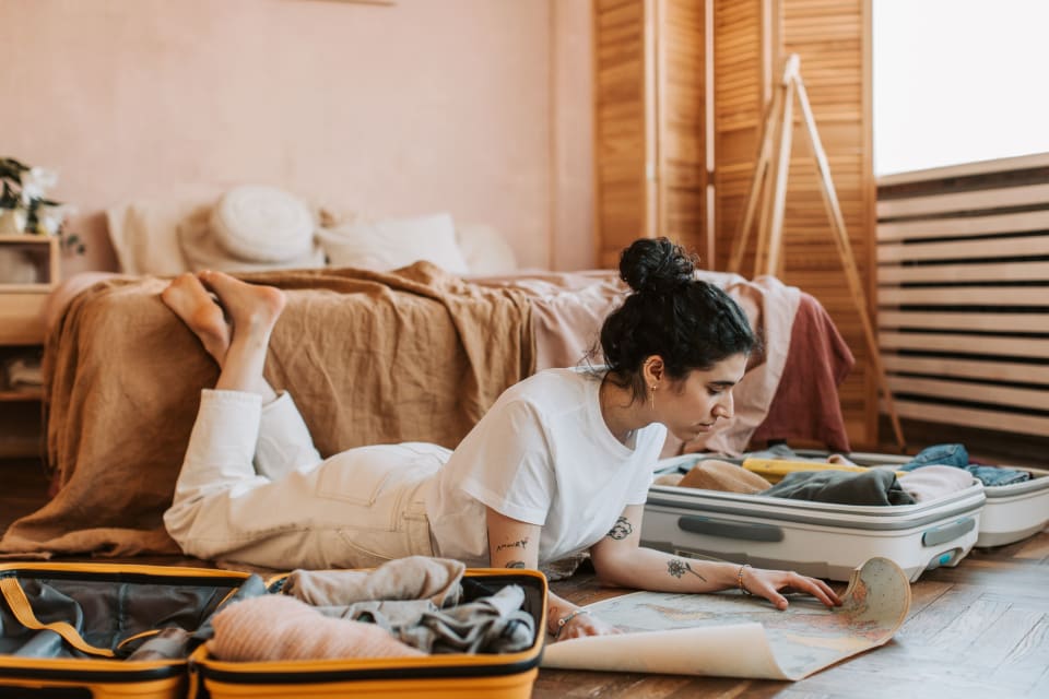 Woman planning a trip with a map beside open suitcases in a comfortable room.