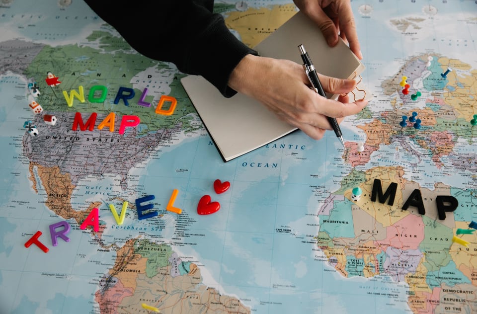 Hands using a notebook and world map to plan an international journey.