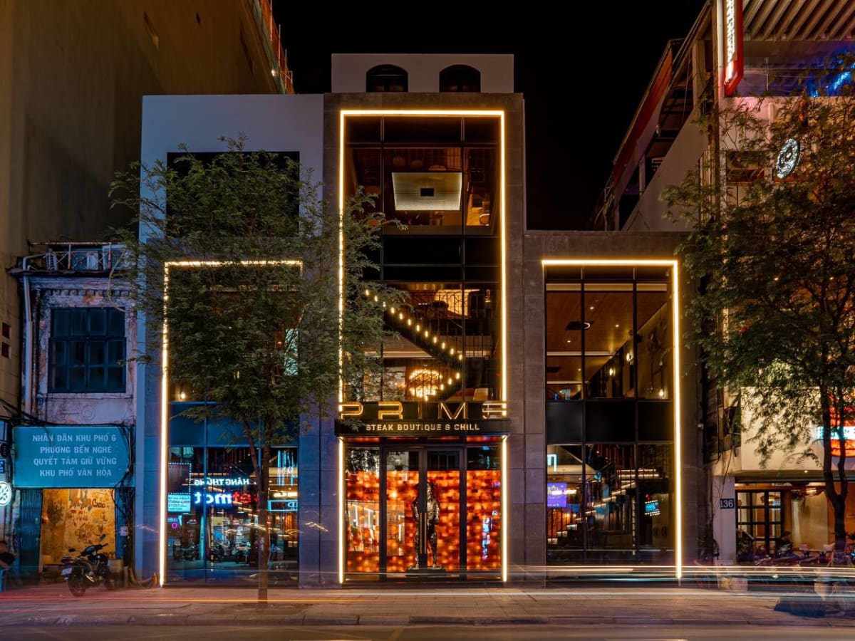 PRIME Steak Boutique & Chill at night, three-storey glass facade revealing the warm interior and dramatic staircase on Pasteur Street