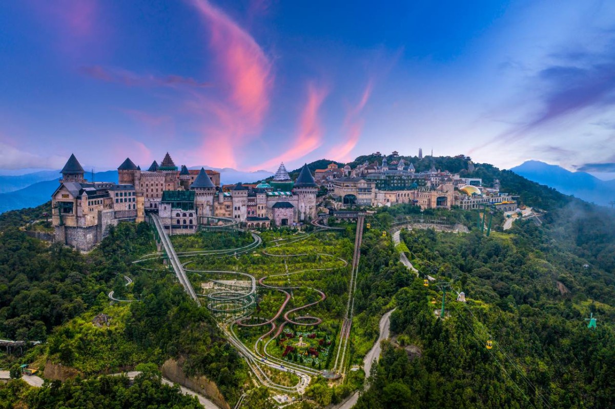 Aerial view of Ba Na Hills French Village at dusk with cable car and mountain backdrop