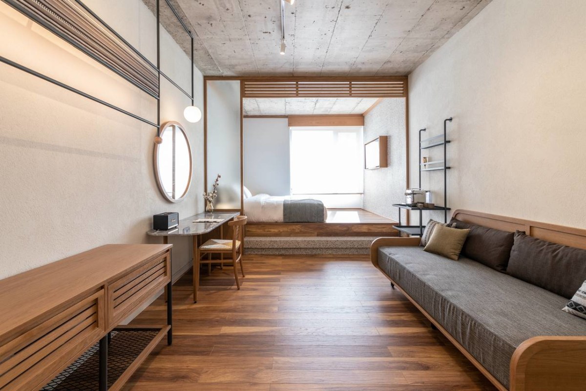 Spacious room at ERGON House Athens with a raised bed platform, warm wooden furnishings and a lounge sofa.